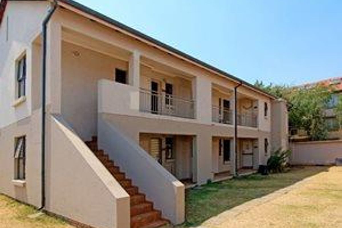 A rear view of a multi-story townhouse complex featuring external staircases, private balconies, and a shared garden area.