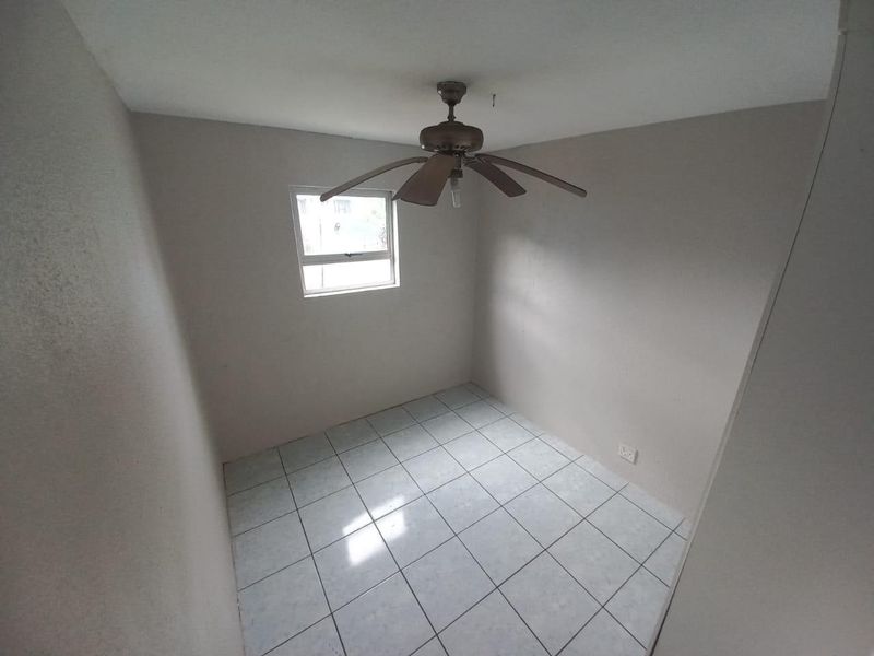 A simple, empty bedroom featuring tiled flooring and a ceiling fan, providing a blank canvas for personalization.