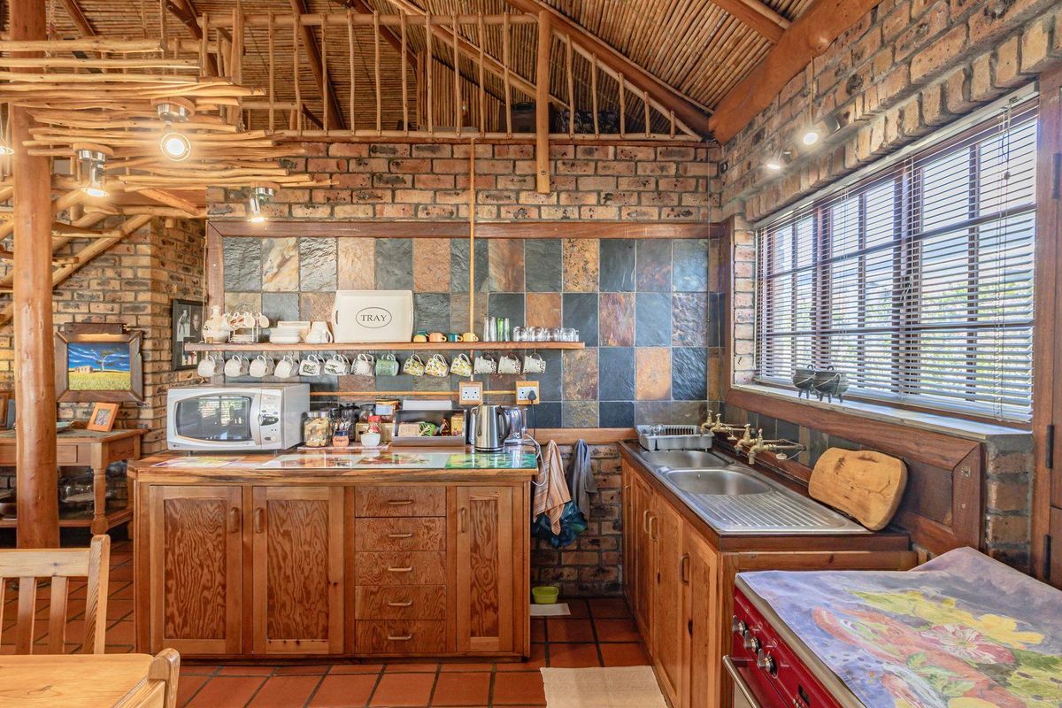 Rustic kitchen featuring exposed brick walls, timber cabinetry, slate tile splashback, and a vaulted thatched ceiling with wooden structural elements.