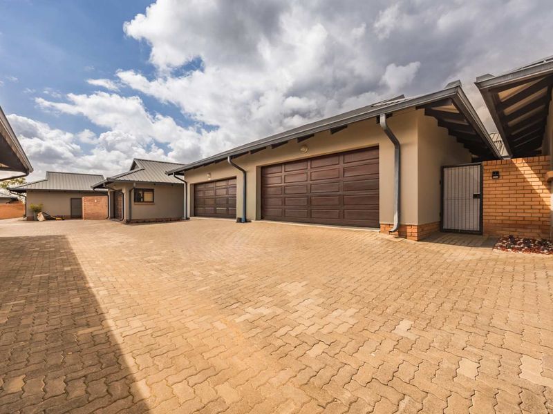 A well-maintained townhouse exterior featuring paved driveway access, multiple garage doors, and brick boundary walling under a pitched roof structure.