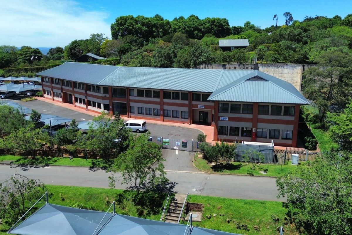 Aerial view of a multi-story office building featuring a metal roof, brick facade, paved driveway, and extensive covered parking facilities within a landscaped setting.