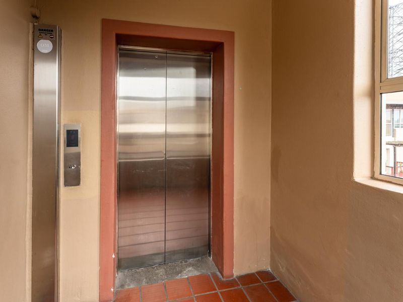 A functional apartment building hallway featuring a stainless steel elevator and tiled flooring with a window providing natural light.