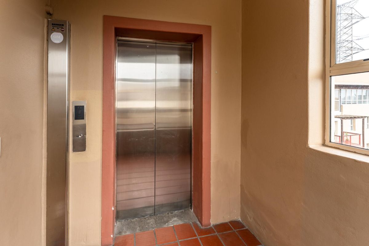 A functional apartment building hallway featuring a stainless steel elevator and tiled flooring with a window providing natural light.