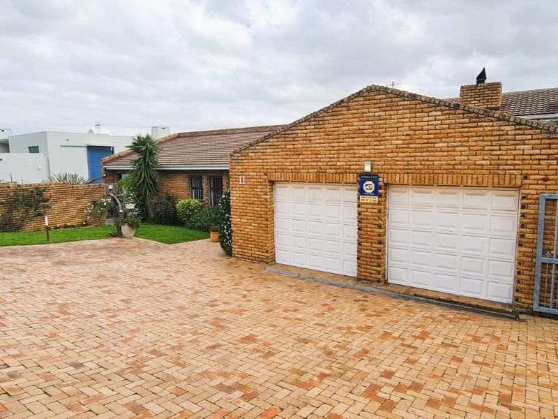 Front exterior view of the property featuring a double garage, paved driveway, and brick facade with secure gated access.