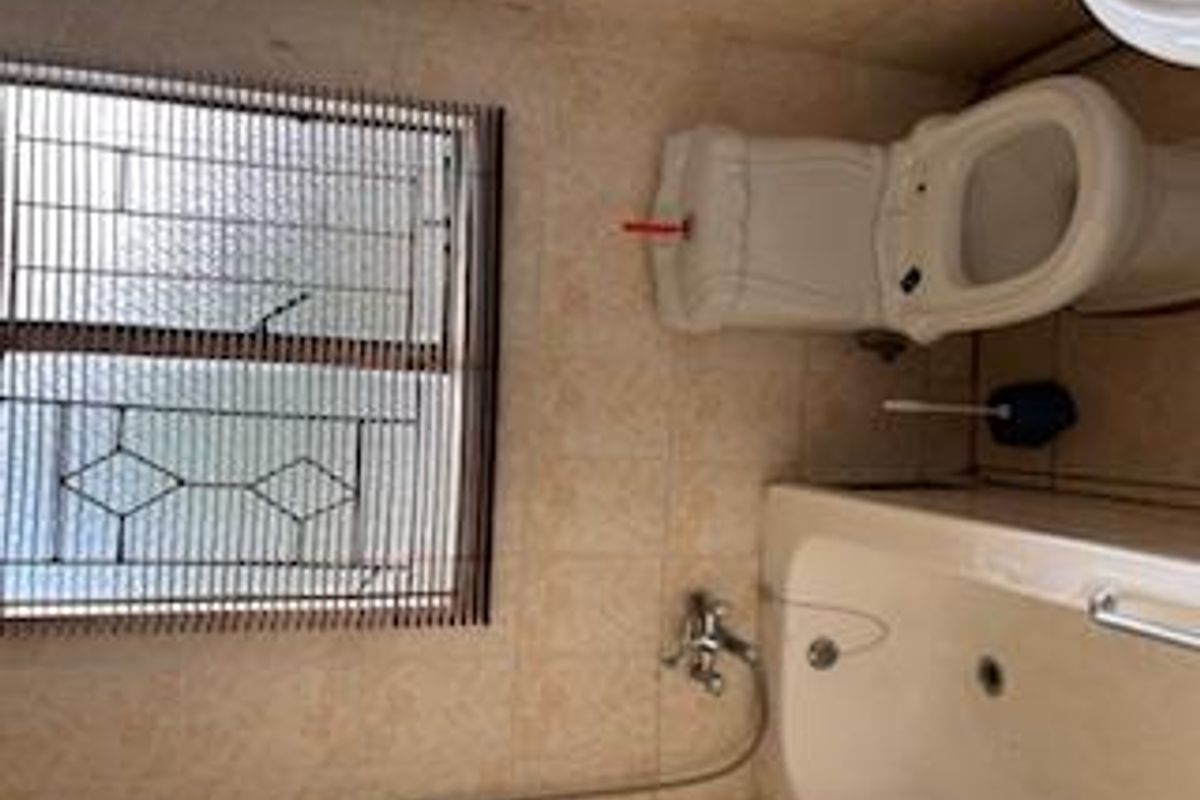 A compact bathroom featuring a standard bathtub, toilet, and a window with security bars, finished with neutral wall and floor tiles.