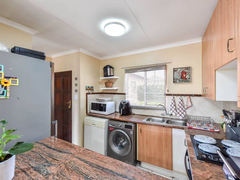 A functional kitchen featuring granite countertops, built-in cabinetry, a double basin sink, and an electric hob with a tiled backsplash.