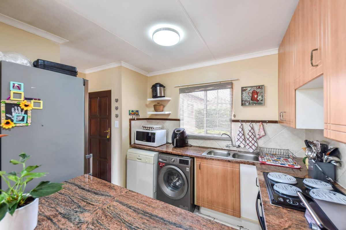 A functional kitchen featuring granite countertops, built-in cabinetry, a double basin sink, and an electric hob with a tiled backsplash.