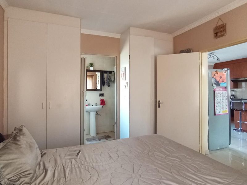 Bedroom featuring built-in cupboards and an en-suite bathroom with a pedestal basin, with direct access to the kitchen area.