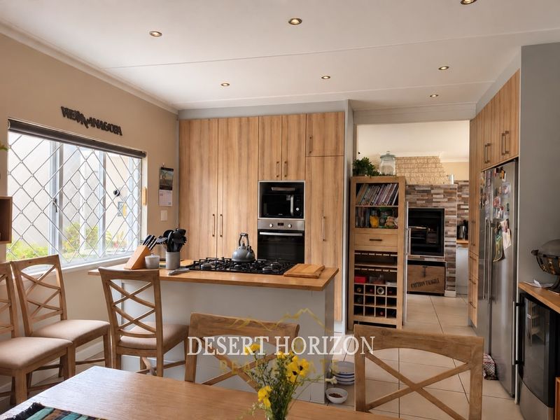 Modern kitchen featuring wood-look cabinetry, built-in oven, gas hob, and tiled flooring, with an open-plan layout leading to an adjacent living area.