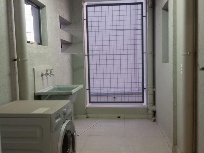 A functional laundry area featuring a utility sink, tiled flooring, and exposed plumbing, secured with a metal grille on the window.