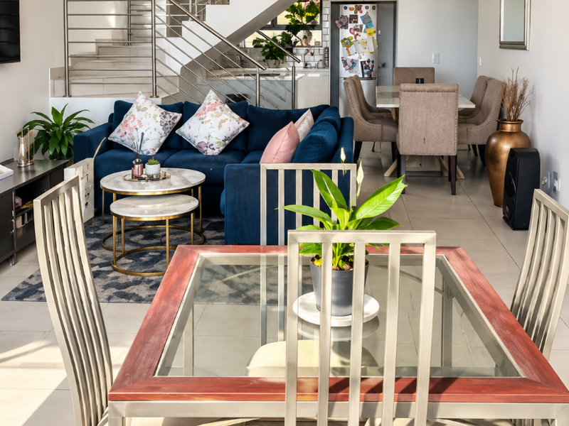 An open-plan living and dining area featuring a modern staircase with stainless steel balustrades, tiled flooring, and recessed lighting throughout the space.