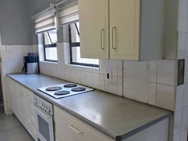 A functional kitchen featuring built-in cabinetry, a laminate countertop, and an integrated electric hob and oven, with tiled backsplash and window blinds.