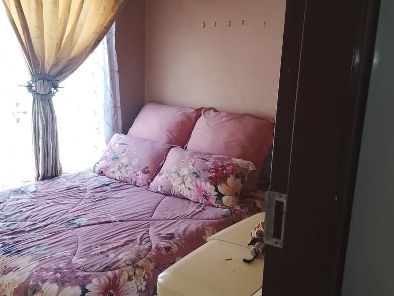 A compact bedroom featuring tiled flooring and natural light through window curtains, requiring cosmetic updates to the wall finishes and door frame.