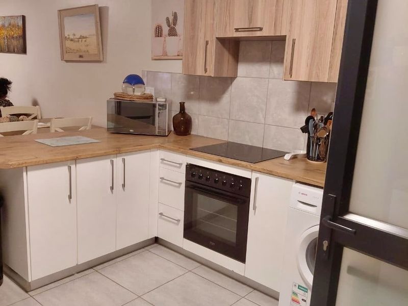 A functional kitchen featuring light wood-tone upper cabinets, white lower cabinetry, laminate countertops, and integrated appliances including an oven, hob, and washing machine.