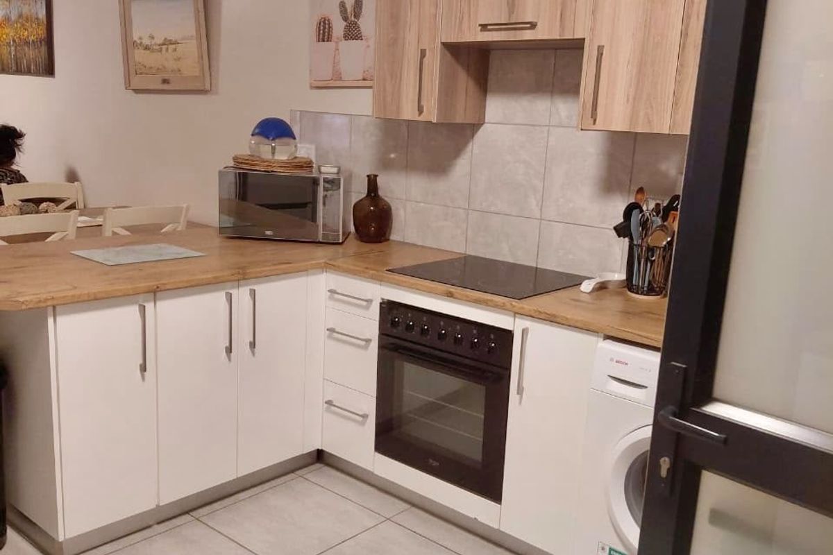A functional kitchen featuring light wood-tone upper cabinets, white lower cabinetry, laminate countertops, and integrated appliances including an oven, hob, and washing machine.