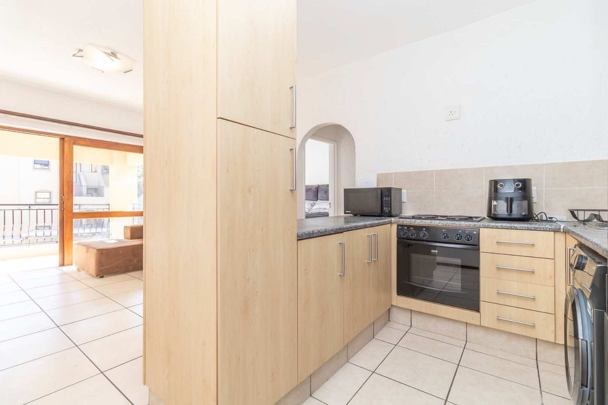 A functional kitchen featuring light wood cabinetry, granite countertops, a built-in oven and hob, and tiled flooring, with an open-plan flow to the living area.