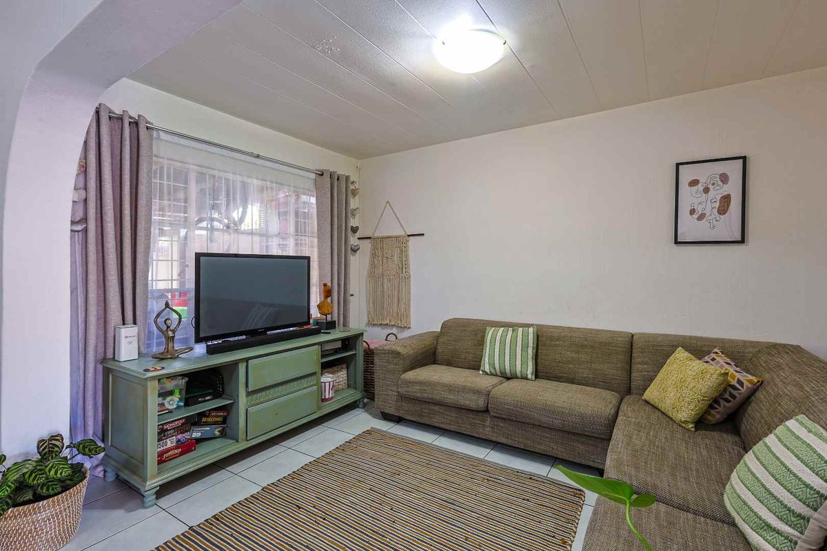 A comfortable living room featuring tiled flooring, a large window with curtain tracks, and a central ceiling light fixture.