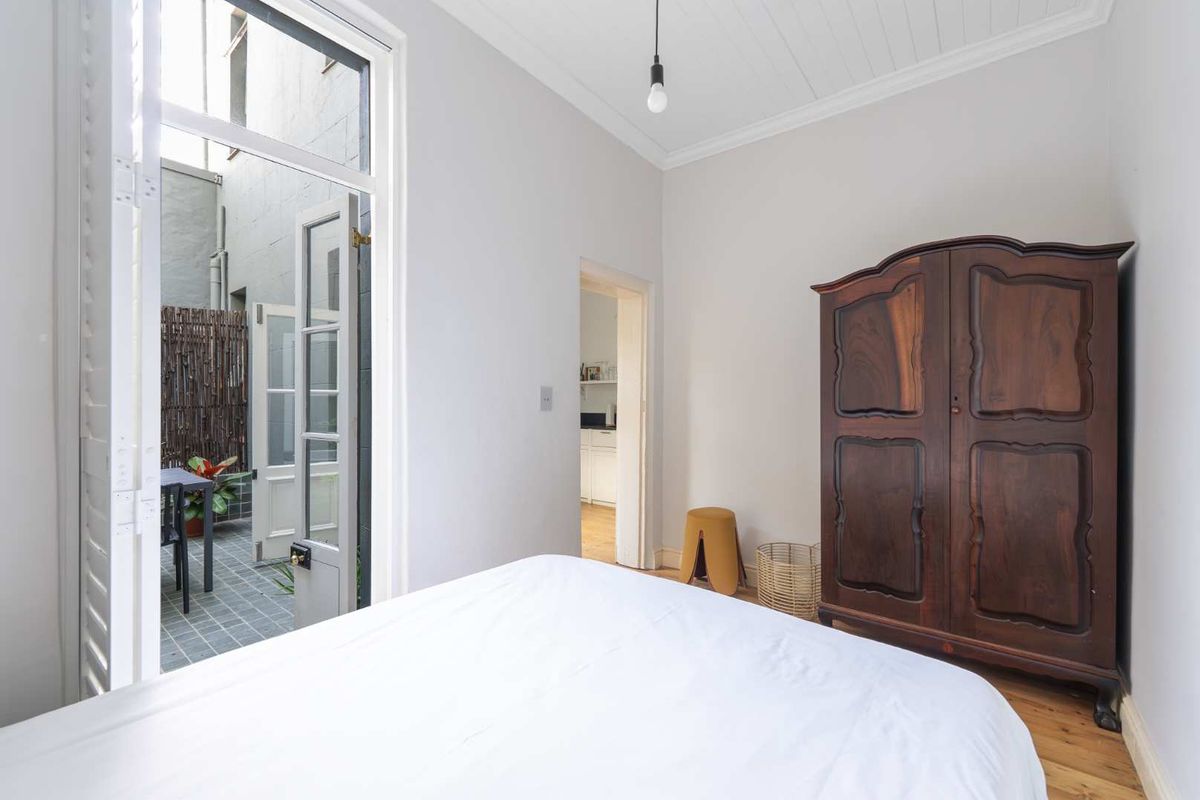 A bright bedroom featuring timber flooring, tongue and groove ceiling, and direct access to a private courtyard through classic french doors.