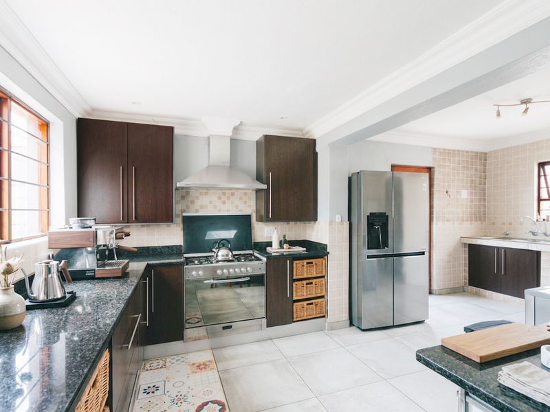 Spacious open-plan kitchen featuring dark wood cabinetry, granite countertops, stainless steel appliances, and a connected scullery area with tiled finishes.
