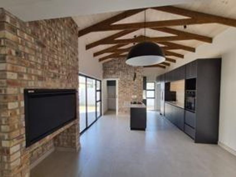 Spacious open-plan living and kitchen area featuring exposed timber beams, a striking brick fireplace, and sleek modern cabinetry in a contemporary design.