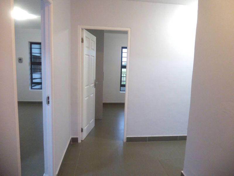 A clean, empty hallway with tiled flooring and white walls, providing access to adjacent rooms through internal doorways.