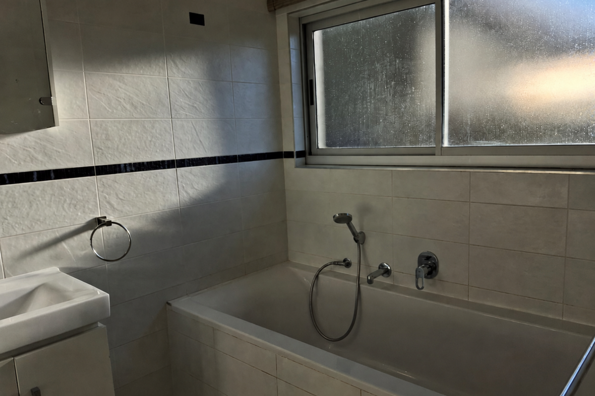 A functional bathroom featuring a built-in bathtub with handheld shower attachment, vanity basin, and tiled walls with a decorative border.