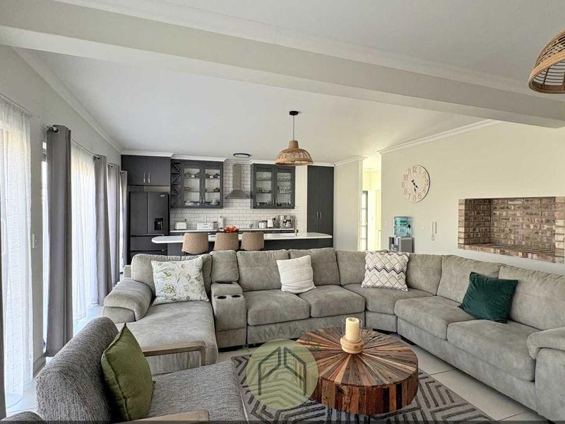 Spacious open-plan living area featuring a modern kitchen with dark cabinetry, subway tile backsplash, and a cozy exposed brick fireplace.