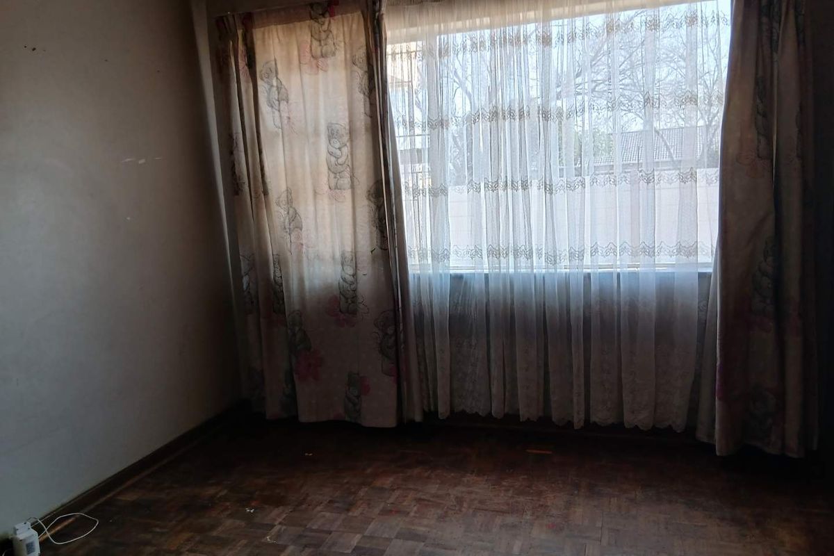 An empty bedroom featuring original parquet flooring and large windows with existing curtain rails, requiring cosmetic updates to restore its appeal.