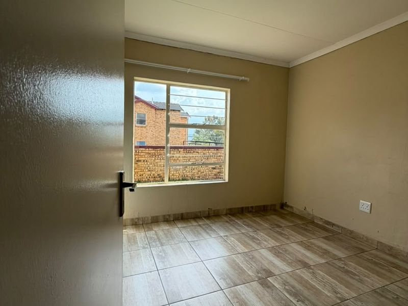 A vacant bedroom featuring tiled flooring, neutral wall tones, and an aluminium-framed window, offering a clean canvas for personalization.
