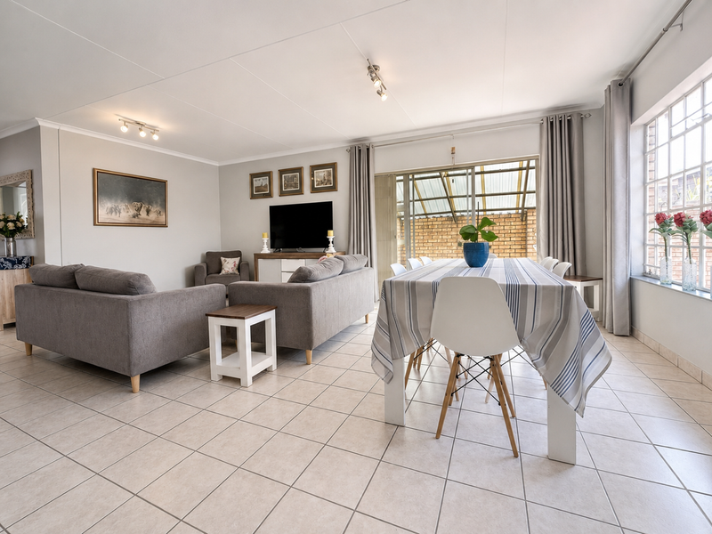 Spacious open-plan living and dining area featuring neutral tiled flooring, large grid-pattern windows, and sliding glass doors leading to an outdoor patio.