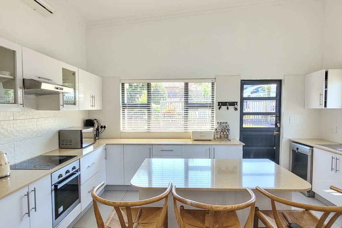 Modern kitchen featuring white cabinetry, stone countertops, a central island, built-in oven, hob, extractor fan, and direct access to the exterior.