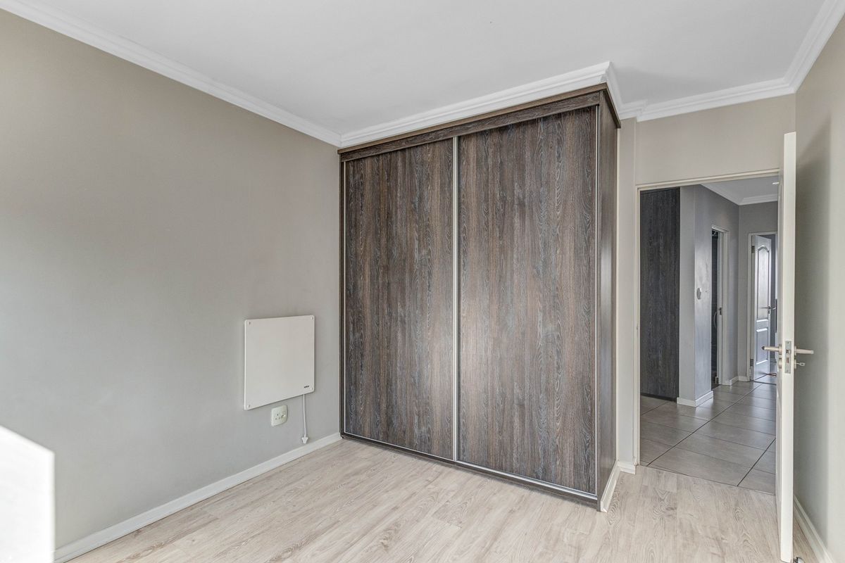 A bright, empty bedroom featuring modern wood-grain built-in wardrobes, light laminate flooring, and a wall-mounted heater.