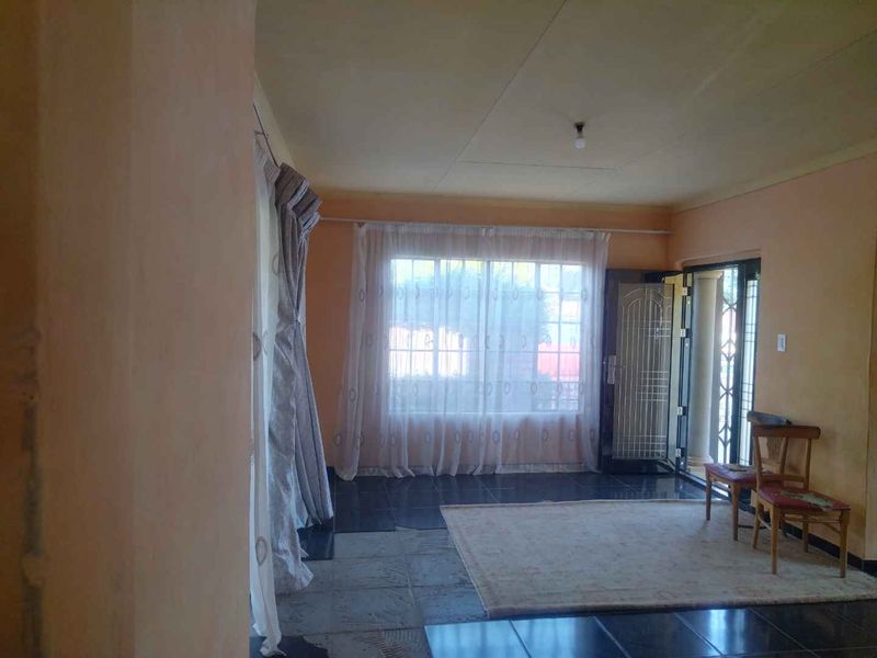 A living room area featuring dark tiled flooring, a sliding door with a security gate, and natural light through large windows.