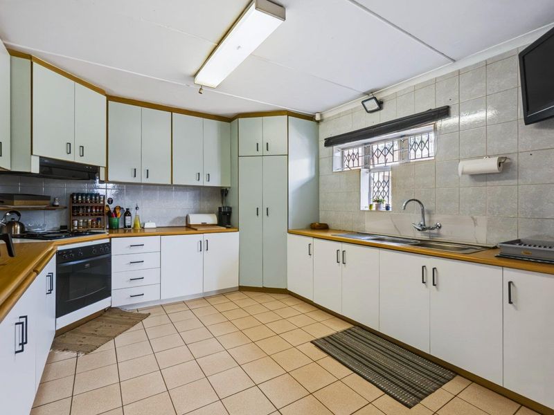 Functional kitchen featuring ample built-in cabinetry, laminate countertops, a stainless steel sink, and integrated cooking appliances with tiled flooring and backsplash.