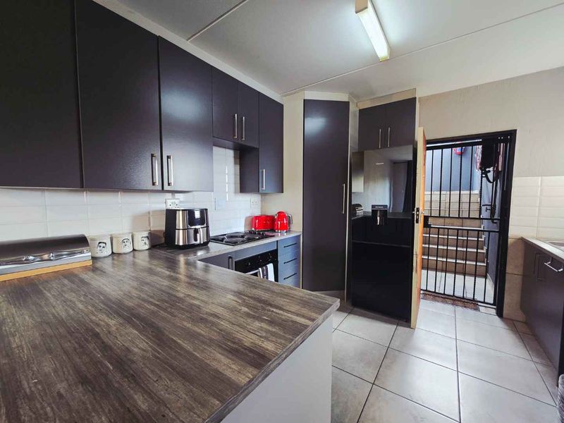Modern kitchen featuring dark cabinetry, wood-look laminate countertops, a gas hob, and tiled flooring, with direct access to an exterior security gate.