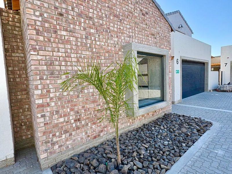 Front exterior view of a modern townhouse featuring a brick facade, paved driveway, and a secure garage.