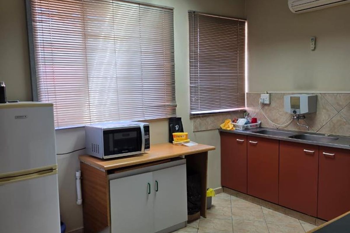 A functional office kitchenette featuring built-in cabinetry, a stainless steel sink, wall-mounted water dispenser, and integrated air conditioning unit.