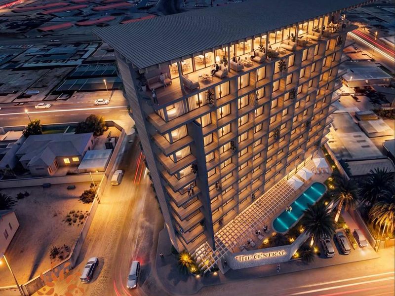 Aerial night view of a modern high-rise hotel building featuring a swimming pool, rooftop terrace, and balconies.