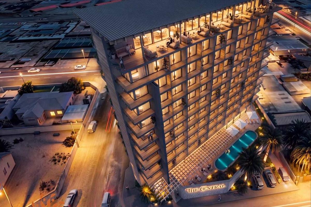 Aerial night view of a modern high-rise hotel building featuring a swimming pool, rooftop terrace, and balconies.