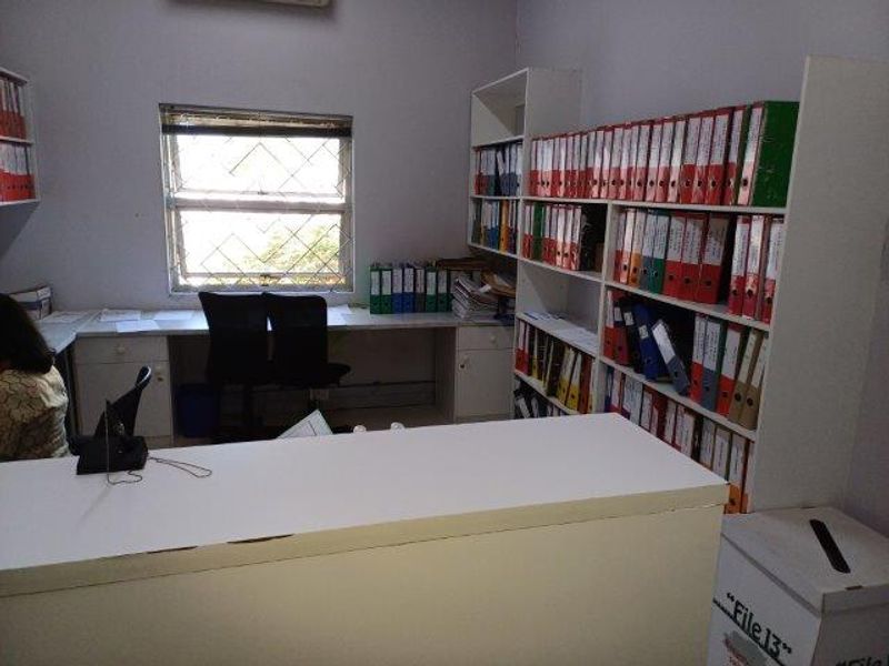 A functional office space featuring extensive built-in shelving for document storage and a built-in desk area with security bars on the window.