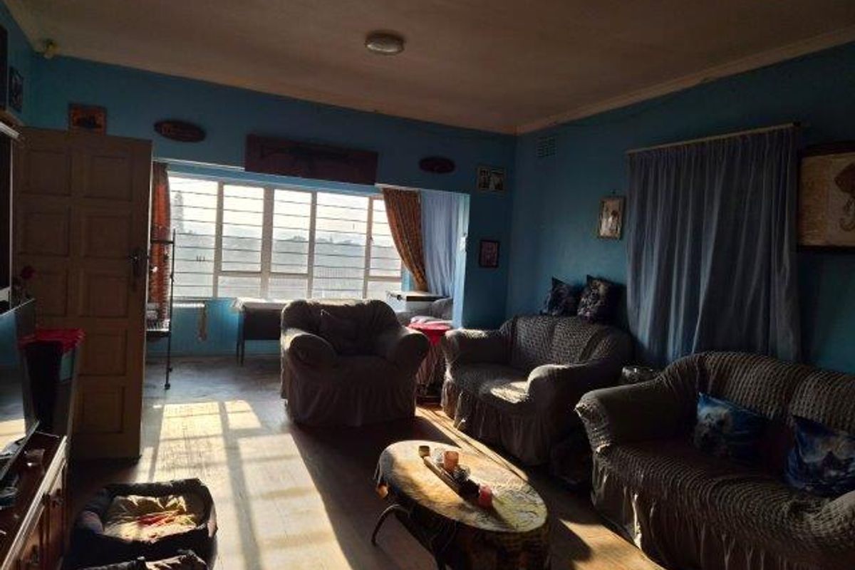 A living room featuring large multi-pane windows, timber flooring, and coved ceilings, offering a bright space with potential for modernization.
