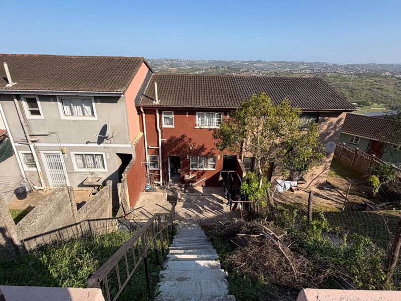 Rear view of the townhouse property featuring a concrete staircase, paved patio area, and elevated views of the surrounding landscape.