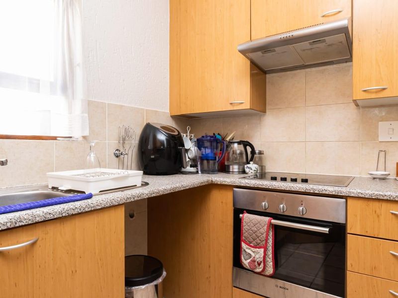 A functional kitchen featuring light wood-finish cabinetry, granite-look countertops, a built-in oven, electric hob, and a stainless steel sink with tiled splashback.