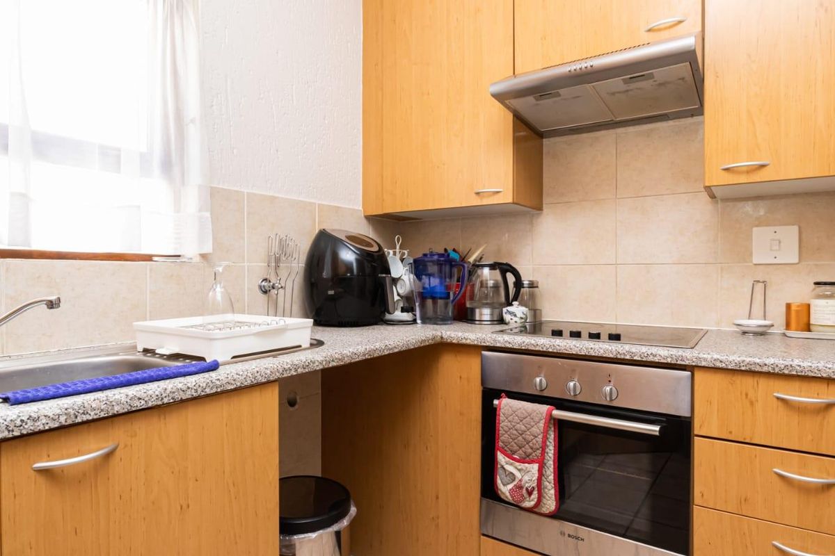 A functional kitchen featuring light wood-finish cabinetry, granite-look countertops, a built-in oven, electric hob, and a stainless steel sink with tiled splashback.
