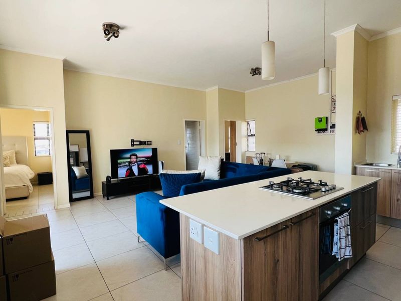 Open-plan living area featuring a modern kitchen with a central island, gas hob, built-in oven, and tiled flooring throughout.