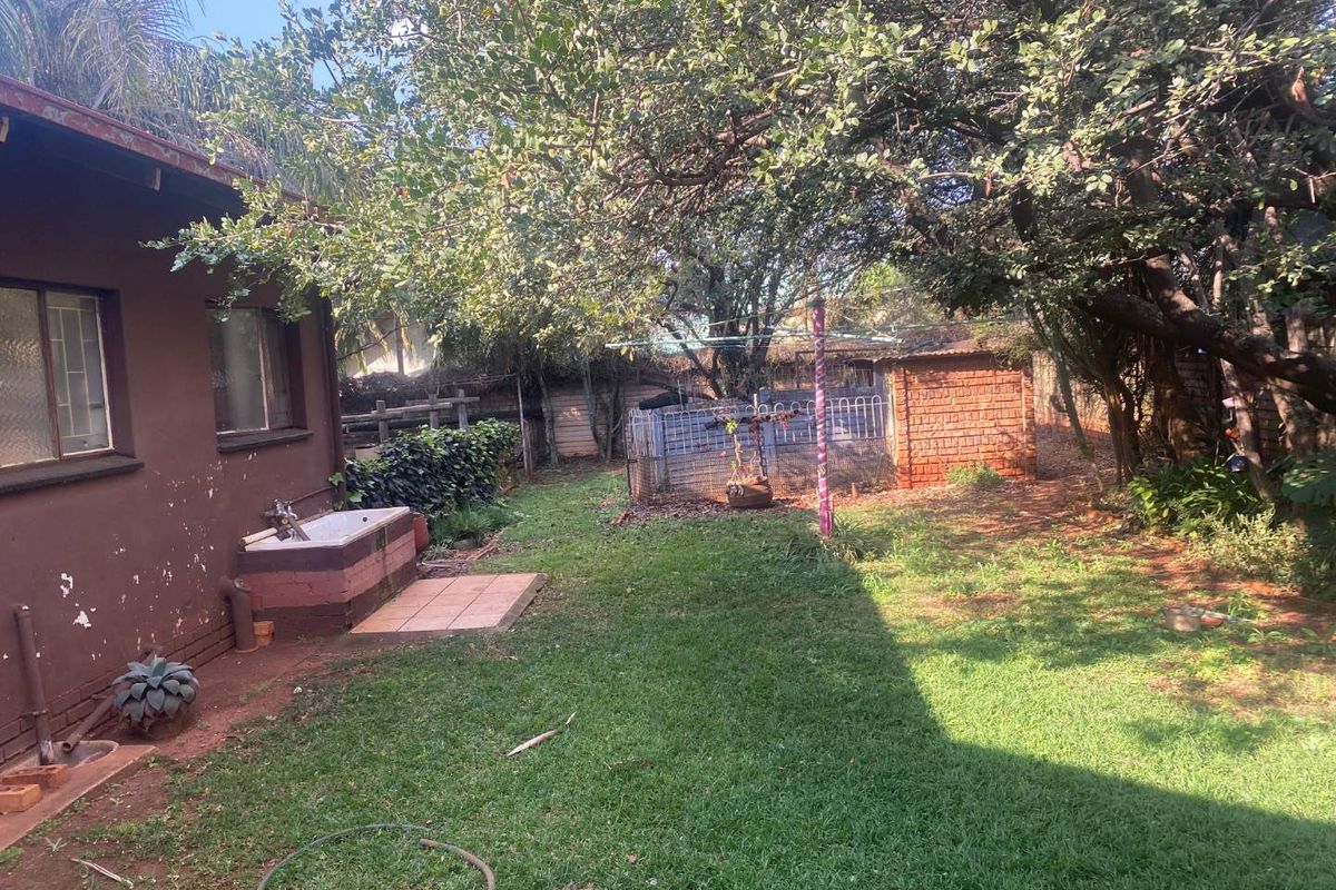 A rear garden area featuring a lawn, mature trees, a small brick outbuilding, and an exterior wall with a built-in utility basin.