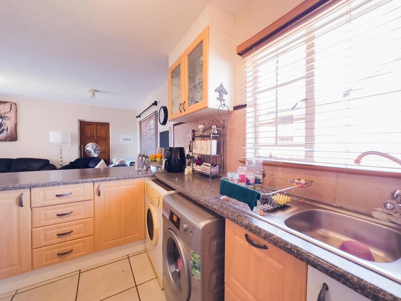 A functional kitchen featuring light wood cabinetry, laminate countertops, a stainless steel sink, and integrated laundry facilities, with natural light from the window.