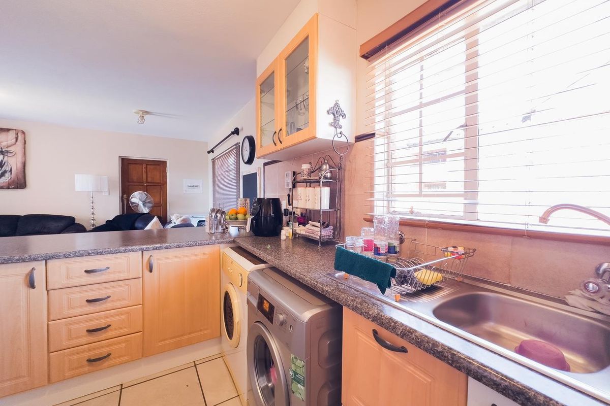 A functional kitchen featuring light wood cabinetry, laminate countertops, a stainless steel sink, and integrated laundry facilities, with natural light from the window.