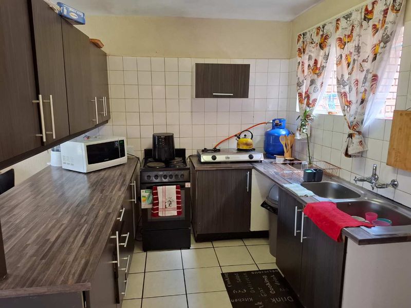 A functional kitchen featuring dark laminate cabinetry, double basin sink, tiled backsplash, and gas hob setup with tiled flooring throughout.
