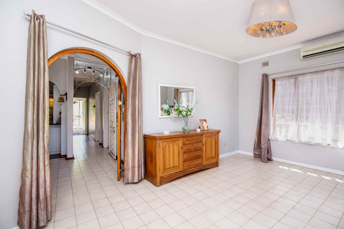 A living room featuring ceramic tile flooring, a decorative archway leading to the hallway, and a wall-mounted split-system air conditioner.